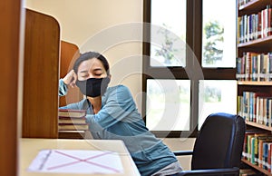 Female student wearing face mask sleeping in a university library