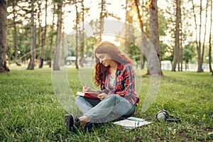 Female student writing in notebook on the grass