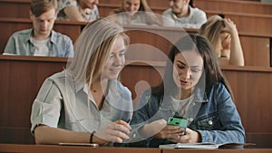 Female students with a smartphone in their hands laughing in the audience during a break for a lecture at the University