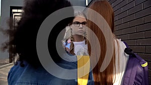 Female students standing front of schoolmate in eyeglasses in backyard, conflict photo