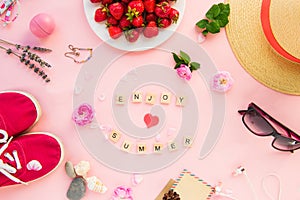 Female summer vacation planning concept - accessories, clothing, flowers and strawberries on pink background. Enjoy Summer letter