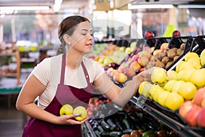 Female supermarket salesperson setting out apples on shelves