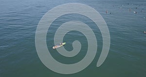 Female surfer paddling with a longboard toward the swimming people in the wavy sea