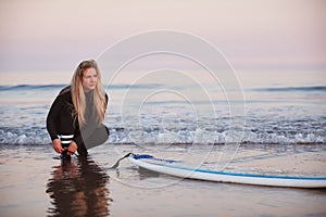 Female Surfer Wearing Wetsuit Attaching Surfboard Leash To Ankle In Waves