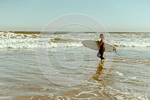Side view of female surfer in wetsuit with his surfboard entering the sea for riding on waves