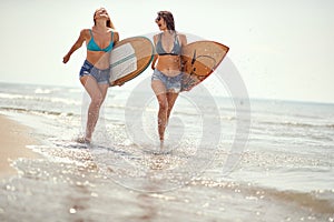 Female surfers running on the beach holding surfboards, laughing