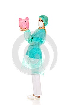 Female surgeon doctor holding piggy bank