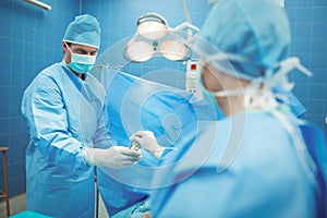 Female surgeon passing surgical tool to her colleague in operation theater