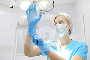 The female surgeon puts on medical protective gloves. Doctor is preparing for surgery in operation room