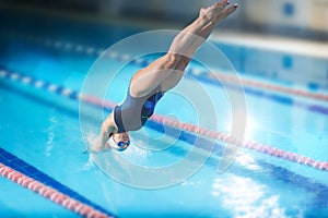 Female swimmer, that jumping into indoor swimming pool.