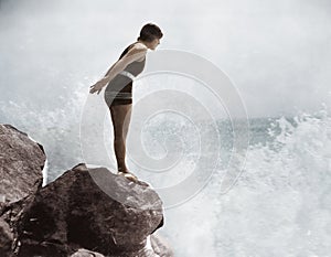 Female swimmer on rock above crashing surf