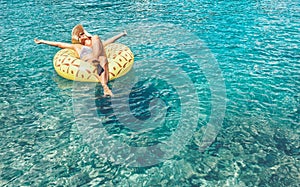 Female swims on inflatable pineapple pool ring in crystal clear sea lagoon