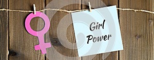 Female symbol cut out of paper and sticky note with the inscription `girl power` attached with a clothespin to a rope on a woode