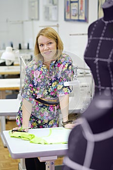 Female tailor stands near table with tailoring