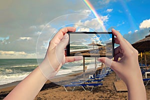 Female taking picture on mobile phone of double rainbow over ocean and tropical beach