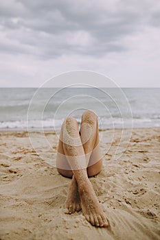 Female tanned legs with sand on smooth skin closeup on beach. Beautiful authentic and creative image. Young woman relaxing on