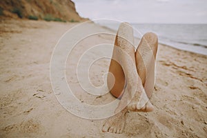 Female tanned legs with sand on smooth skin closeup on beach. Beautiful authentic and creative image. Young woman relaxing on