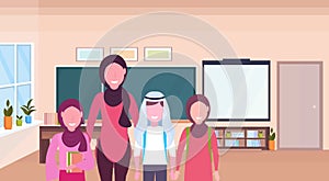 Female teacher with arab pupils in hijab standing over chalkboard modern school classroom interior muslim arabian