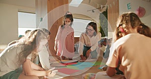 A female teacher with a bob hairstyle in glasses and a white shirt conducts a drawing lesson for preschool children. A