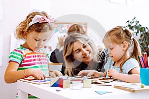 Female teacher with children have fun in development center. Writing, reading lessons and learn ABC by cubes. Adoption