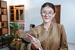 female teacher in civil servant uniform wearing glasses smiling while carrying a book