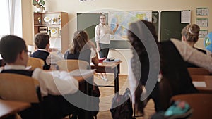 Female teacher in class near the map of the world communicates with students, asks questions and explains.