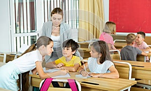 Female teacher controlling group work of interested tweens at lesson