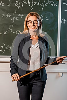 Female teacher in formal wear with wooden pointer explaining mathematical equations