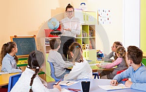 Female teacher giving geography lesson in classroom, showing pupils globe