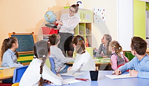 Female teacher giving geography lesson in classroom, showing pupils globe