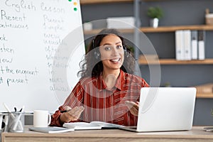 Female teacher in headphones sitting at desk talking to camera