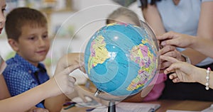 Female teacher with kids in geography class looking at globe. Side view of group of diverse happy school kids with globe