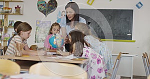 Female teacher with kids in geography class looking at globe. Side view of group of diverse happy school kids with globe