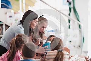 Female teacher with kids in geography class looking at globe. Side view of group of diverse happy school kids with globe