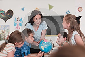 Female teacher with kids in geography class looking at globe. Side view of group of diverse happy school kids with globe