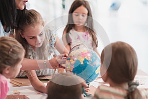 Female teacher with kids in geography class looking at globe. Side view of group of diverse happy school kids with globe
