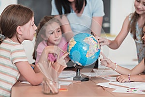 Female teacher with kids in geography class looking at globe. Side view of group of diverse happy school kids with globe