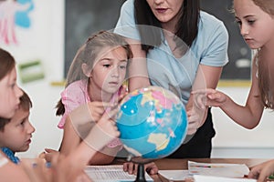 Female teacher with kids in geography class looking at globe. Side view of group of diverse happy school kids with globe