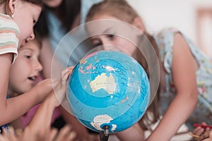 Female teacher with kids in geography class looking at globe. Side view of group of diverse happy school kids with globe