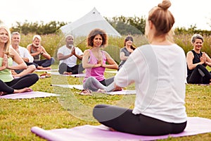 Female Teacher Leading Group Of Mature Men And Women In Class At Outdoor Yoga Retreat