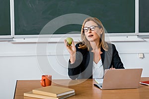 Female teacher sitting at computer desk and holding apple
