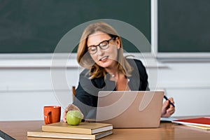 Female teacher sitting at computer desk and reaching for apple