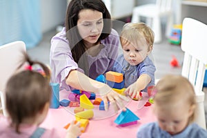 Female teacher sitting at table in playroom with three kindergarten children constructing