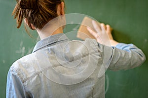 Female teacher or a student cleaning blackboard with a sponge.