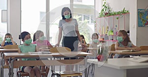 Female teacher wearing face mask at school, teaching children at school classroom. Education back to school health
