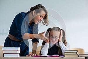 A female teacher yells at a student. Little girl covers her ears with her hands. photo