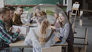 Female team leader brings documents to creative business team. Mixed race group of people meeting in modern office.