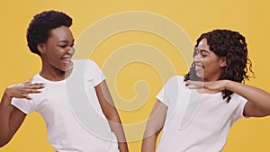 Female teamwork and friendship. Two african american women making fist bump gesture and laughing, orange background,