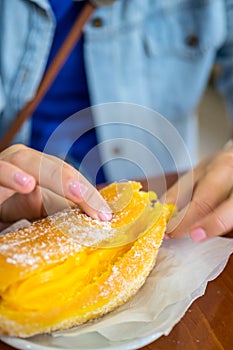 Female tearing portuguese doughnut or Berliner with egg creme and Coffee on brown wooden table in a local Pastelaria photo