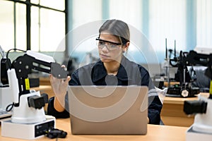 Female technician engineer using laptop checking automatic robotic machine